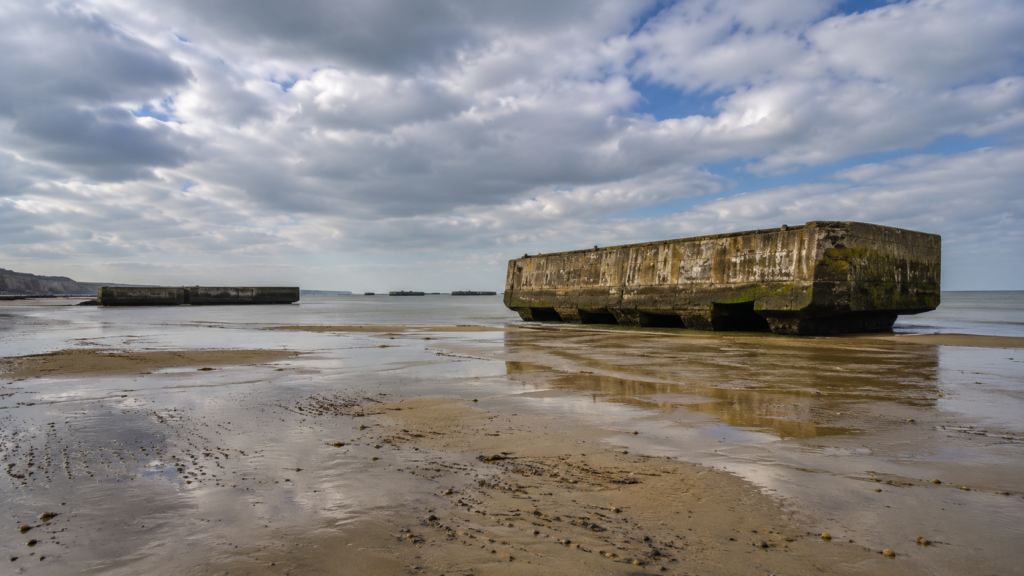 Remains of the WWII Mulberry harbour caissons on the beach at Arromanches at low tide, seen from the shore near the D-Day landing museum.