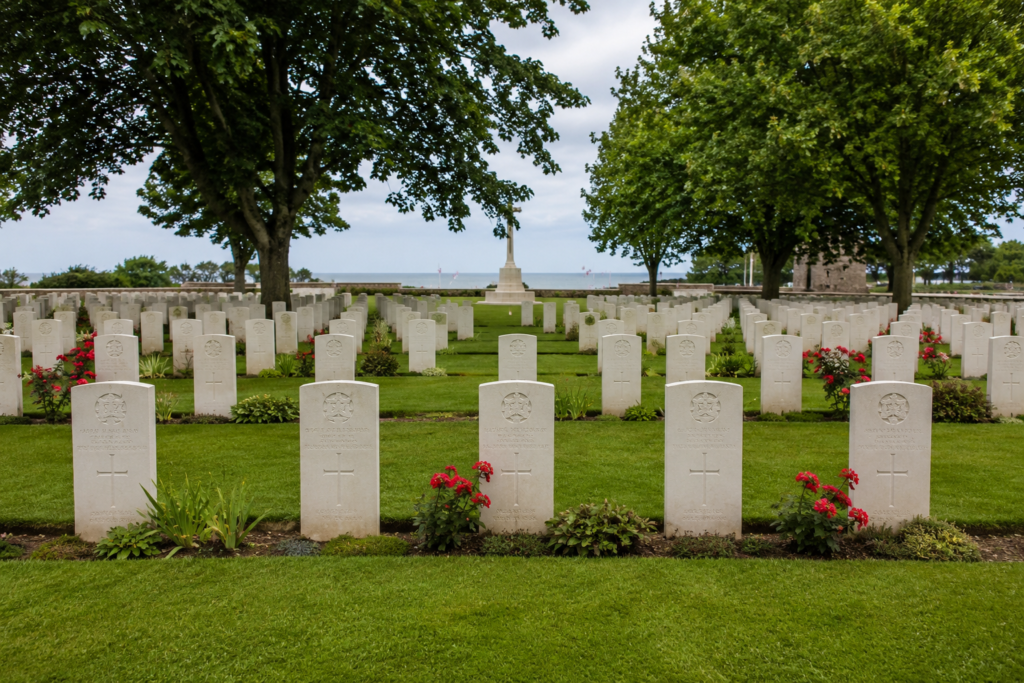 Rows of white headstones beneath maple trees at a Canadian war cemetery near Juno Beach.