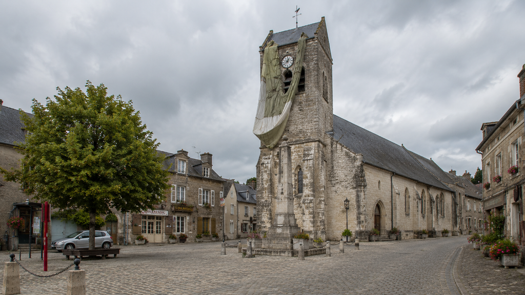 Village church square in Normandy with a parachute caught on the church tower, marking the WWI airborne landing story.
